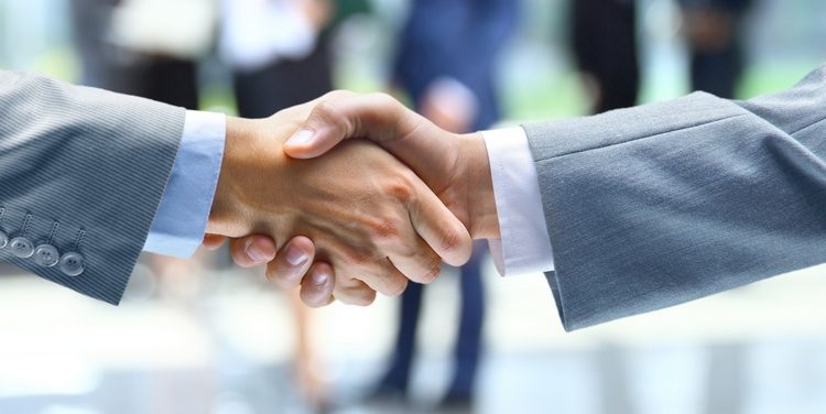 Человек держит младенца на руках и делает рукопожатие.