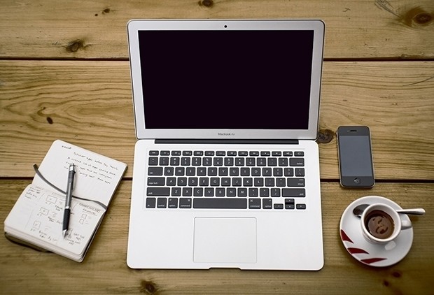 Ноутбук и мобильный телефон на столе с книгой, планшетом и ручкой.