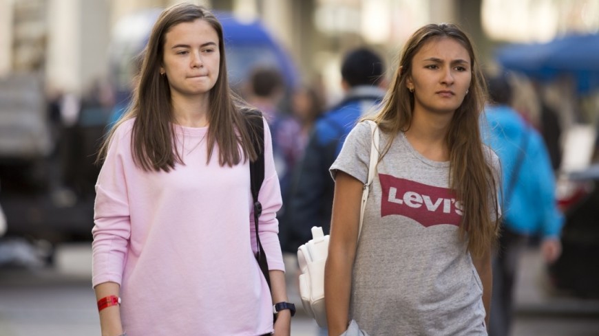 Девушка в подростковом возрасте с сумочкой и часами, идущая мимо постера с головой.