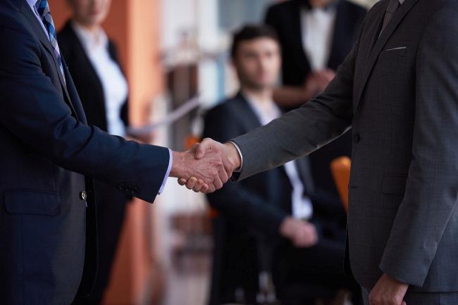 Рука мужчины в костюме, держащего взрослого человека за руку.