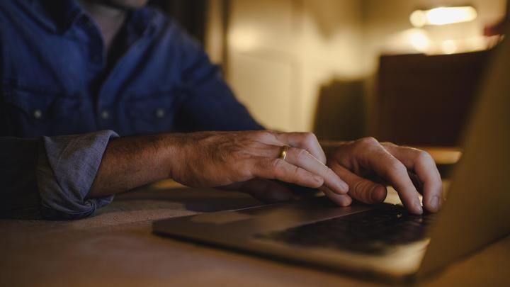 Человек, использующий ноутбук с клавиатурой на фоне компьютерной техники и электроники.