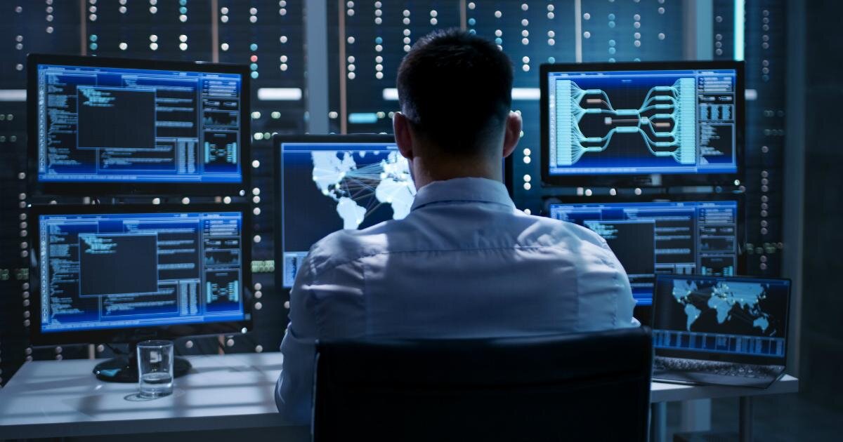 Взрослый мужчина сидит у монитора компьютера, обрабатывает данные, работает.