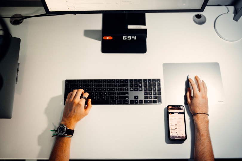 "Man working on laptop and mobile phone at desk with keyboard and phone on table."