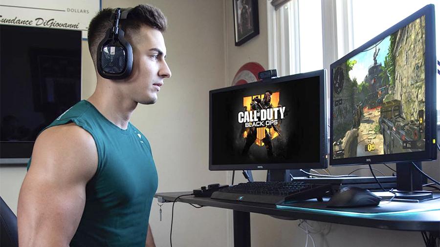 Взрослый мужчина с наушниками играет в видеоигры на мониторе с компьютерной клавиатурой.