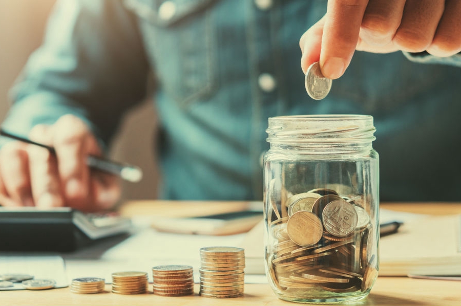 Рука человека держит ручку над стеклянной банкой в стиле масонского флакона.