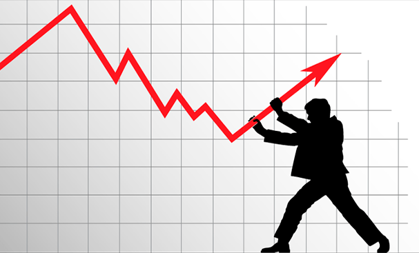 Взрослый мужчина в пальто с капюшоном, стоящий на фоне зеленой листвы.
