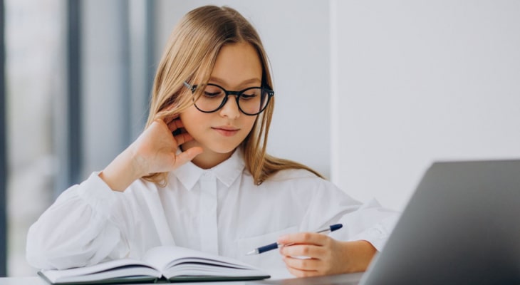 Человек в очках читает книгу на ноутбуке с ручкой рядом.