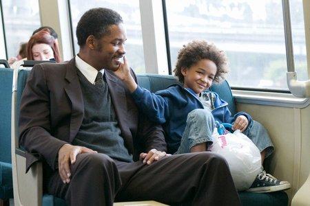 Два человека на диване - одеты в пальто и куртки, смотрят в камеру.