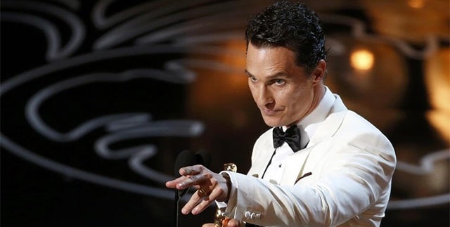 Мужчина в формальной одежде с галстуком, исполняющий сольное выступление перед толпой.