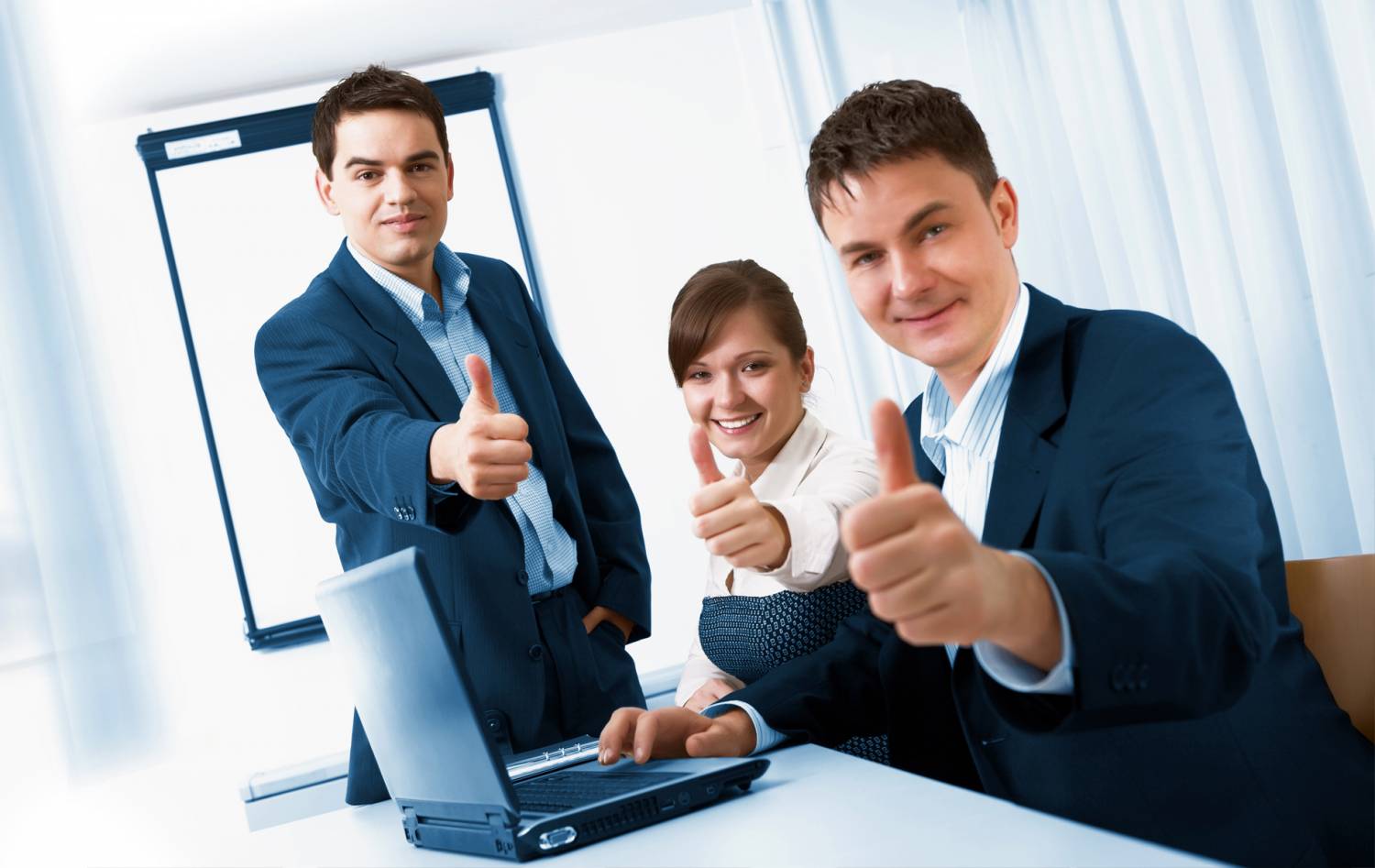 Взрослый мужчина в костюме сидит перед ноутбуком, женщина в фоне.