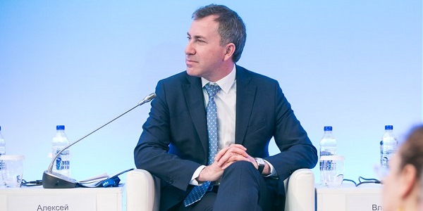 Мужчина в галстуке с микрофоном, в окружении толпы людей и чашкой кофе.