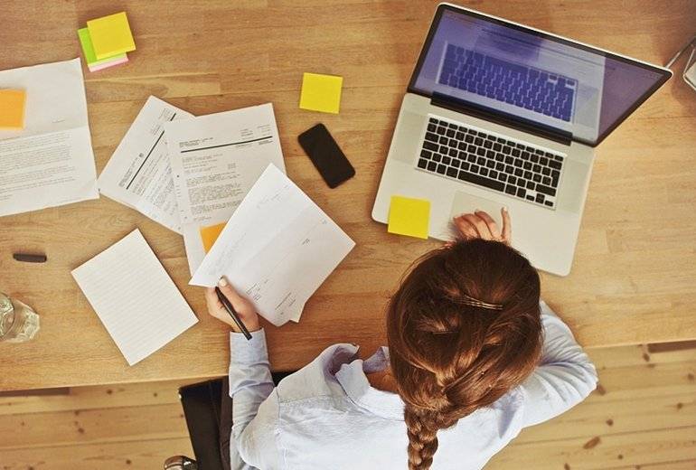 Человек работает за ноутбуком, смотрит на мобильный телефон и документ на компьютере.