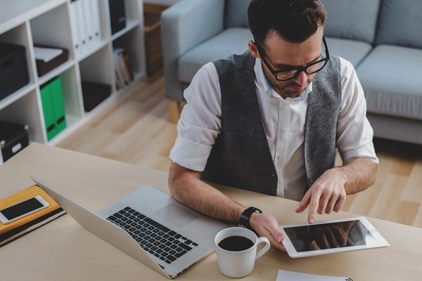 Мужчина на рабочем месте за ноутбуком, рядом с мобильным телефоном, компьютером.