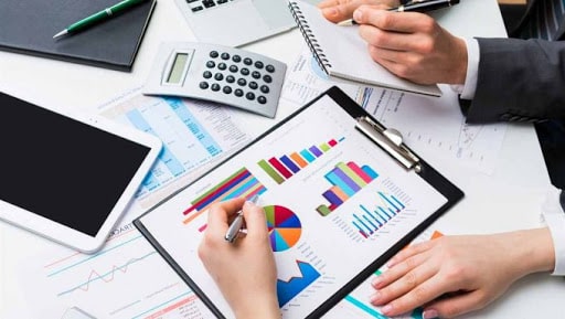 Рука человека, держащего ручку, над книгой с графиком и публикацией.