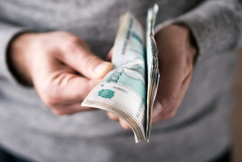 Рука человека держит банку с деньгами: деталь изображения с частями тела и деньгами.