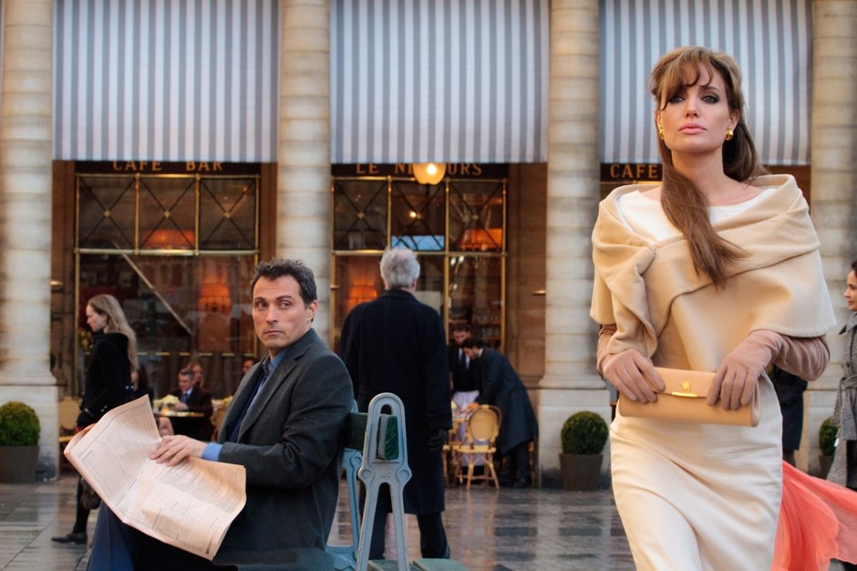 Взрослая женщина в платье с кошельком стоит у растения, мужчина рядом.