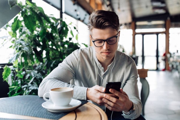 Крупный план на чашку кофе в руках человека, сидящего с телефоном.