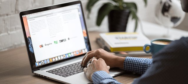 Мужчина работает на ноутбуке возле растения и чашки с кофе.