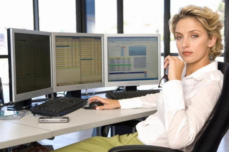 Девушка-подросток сидит за столом с компьютерной клавиатурой, монитором и мобильным телефоном.