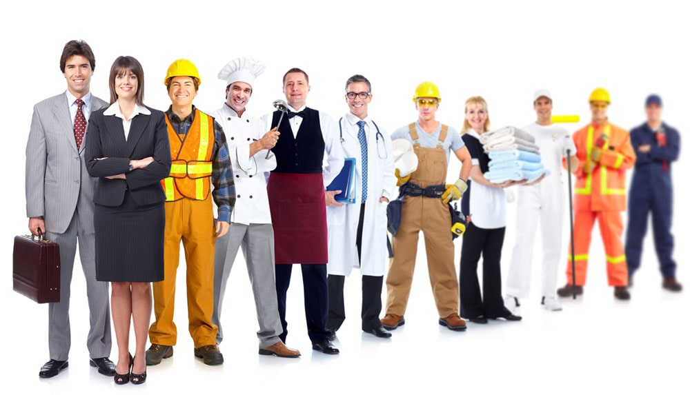 Фото: рабочий в шлеме и перчатках, стоящий среди группы людей, одетых в костюмы.