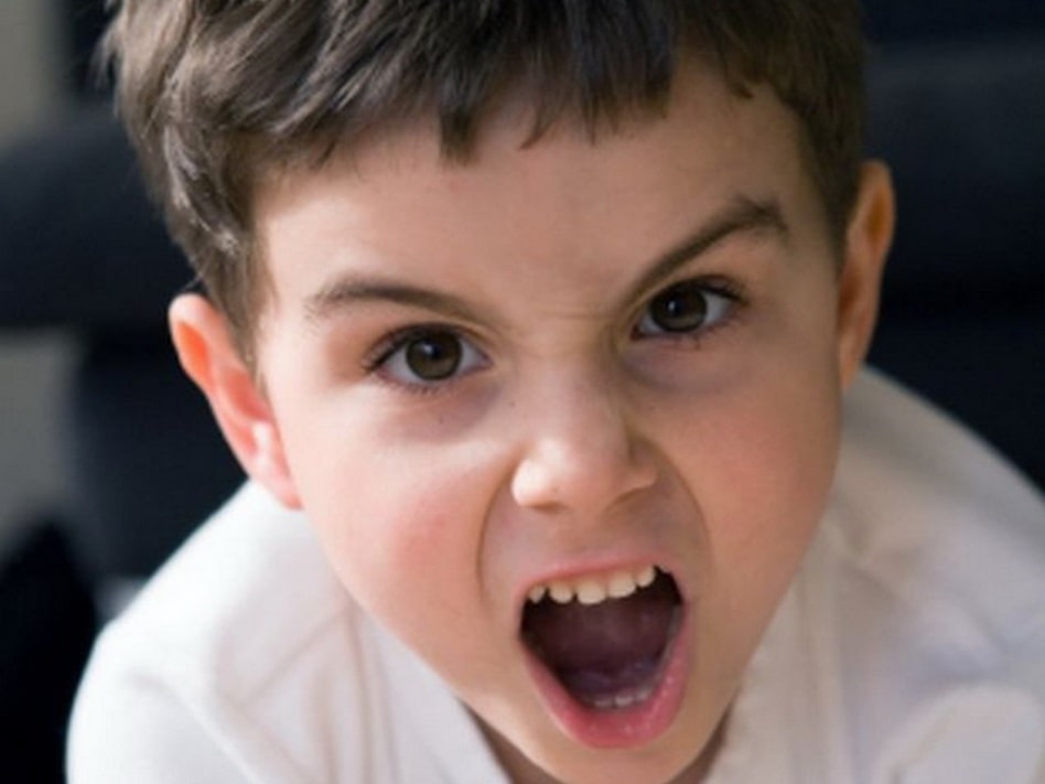 Мальчик-ребенок с серьезным выражением лица кричит и держит голову.