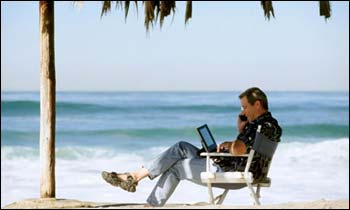 Человек сидит с ПК на пляже, читает, наслаждаясь видом моря.