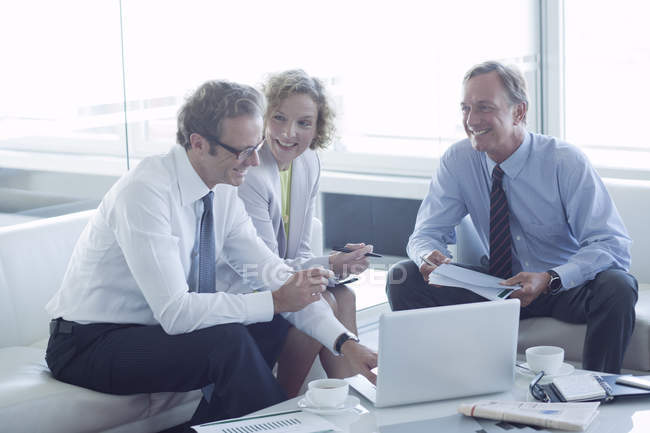 Человек в пальто и рубашке сидит с ноутбуком и чашкой кофе.