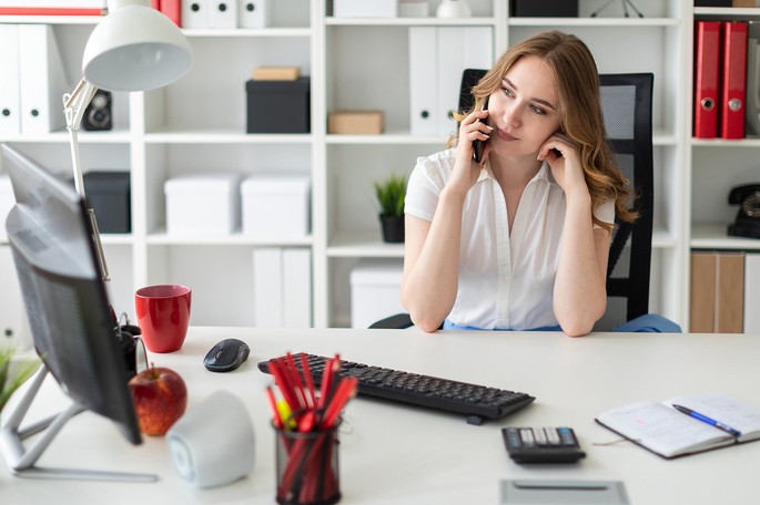 Человек с яблоком на фоне монитора, удерживает ручку, рядом кружка и клавиатура компьютера.