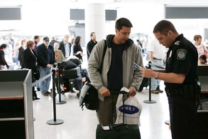 Мужчина-взрослый с сумкой стоит возле монитора в аэропортском терминале.