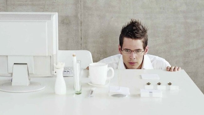 Человек мужского пола скулится в кружке, надев очки, покрывая голову от дождя.