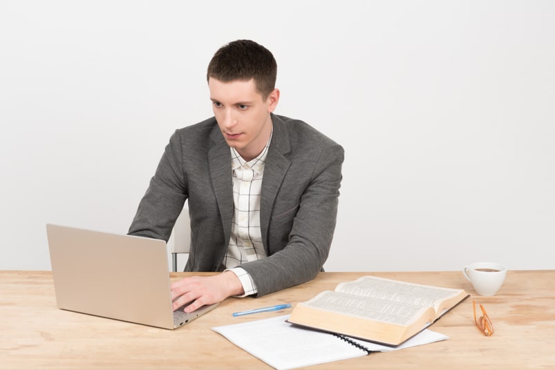 Человек сидит за ноутбуком в офисе, работает с ПК и электроникой.