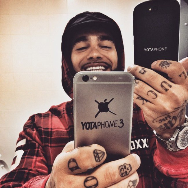 Портрет человека с татуировкой на пальце, держащего мобильный телефон в руке.