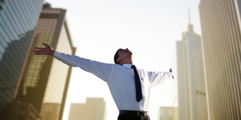 Мужчина в городе на фоне зданий, улыбается, в рубашке и галстуке.