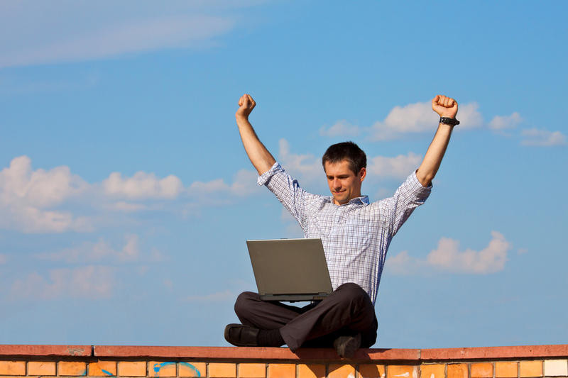 Счастливый мужчина с триумфальным выражением лица, работающий на ноутбуке.