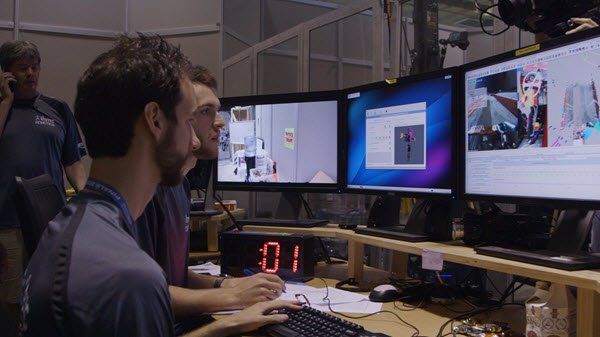 Стол с компьютером, монитором, клавиатурой, электроникой. Персона на фоне.