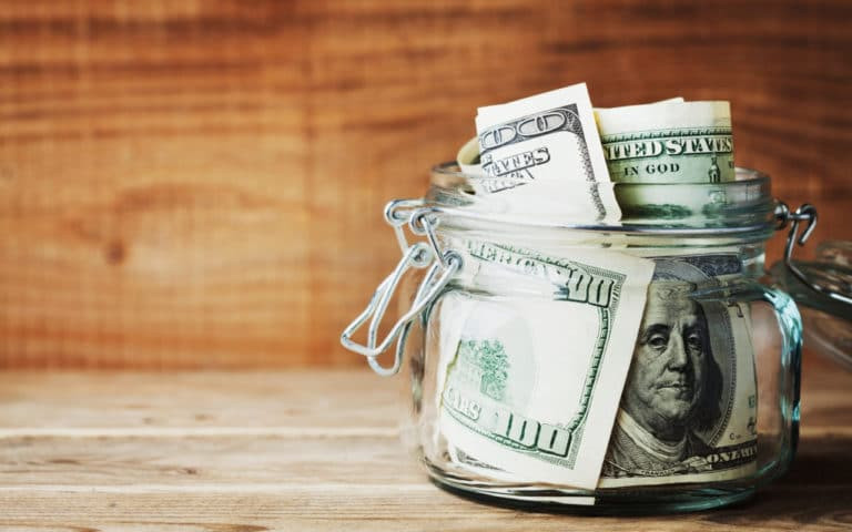 Человек держит джар с деньгами и пластиковый стакан в руке.