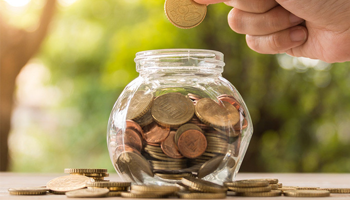 Человек держит банку с деньгами и монетой в руке.