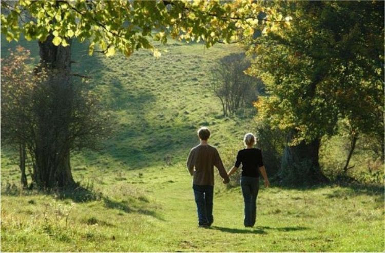 Рука в руке, взрослые мужчина и женщина, идущие по тропинке с растительностью.