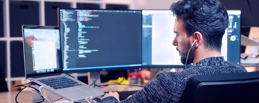 Компьютерная клавиатура на фоне ноутбука с монитором, человек, наушники.