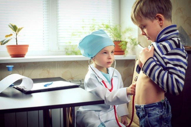 Мальчик в пальто со стетоскопом у растения, в интерьере.