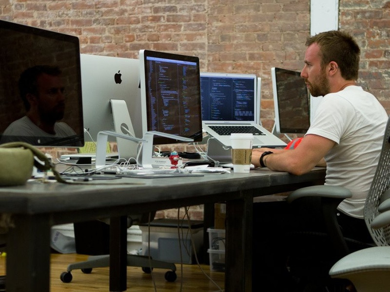 Мужчина работает за компьютером на столе в кабинете с мебелью.