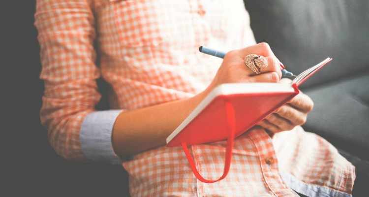 Человек пишет головой ручкой на белом фоне.