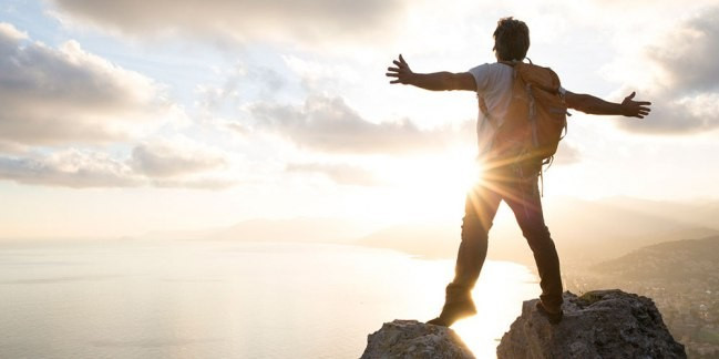 Фотография мужчины, занимающегося хайкингом под ярким солнцем на природе.