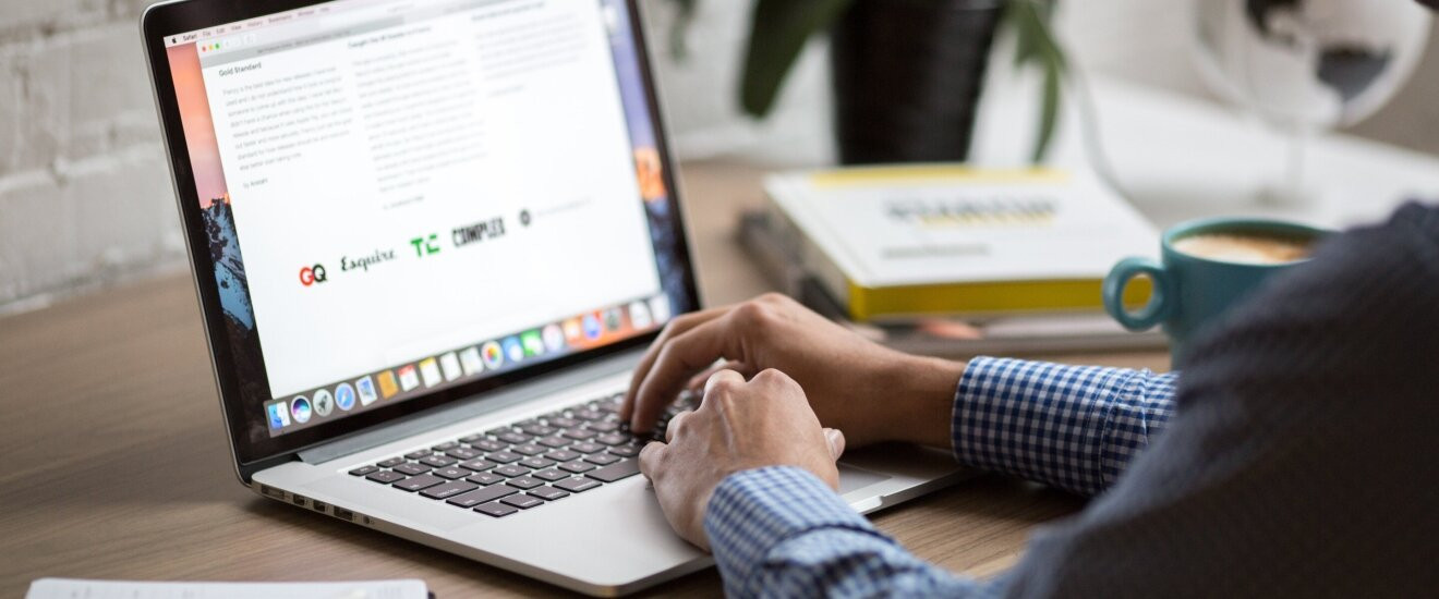 Ноутбук на столе, мужчина пишет на бумаге с чашкой кофе.