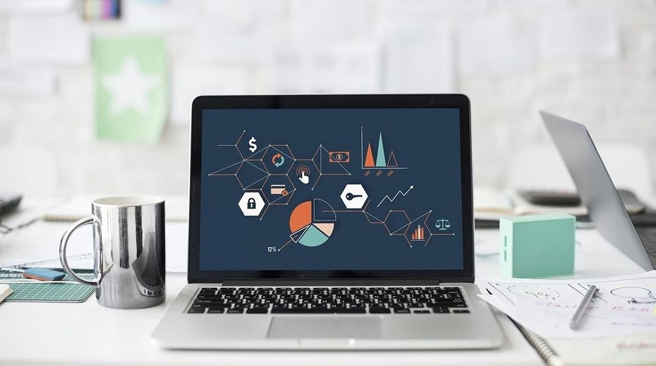 Ноутбук с электроникой, стаканом, ручкой и диаграммой на фоне.