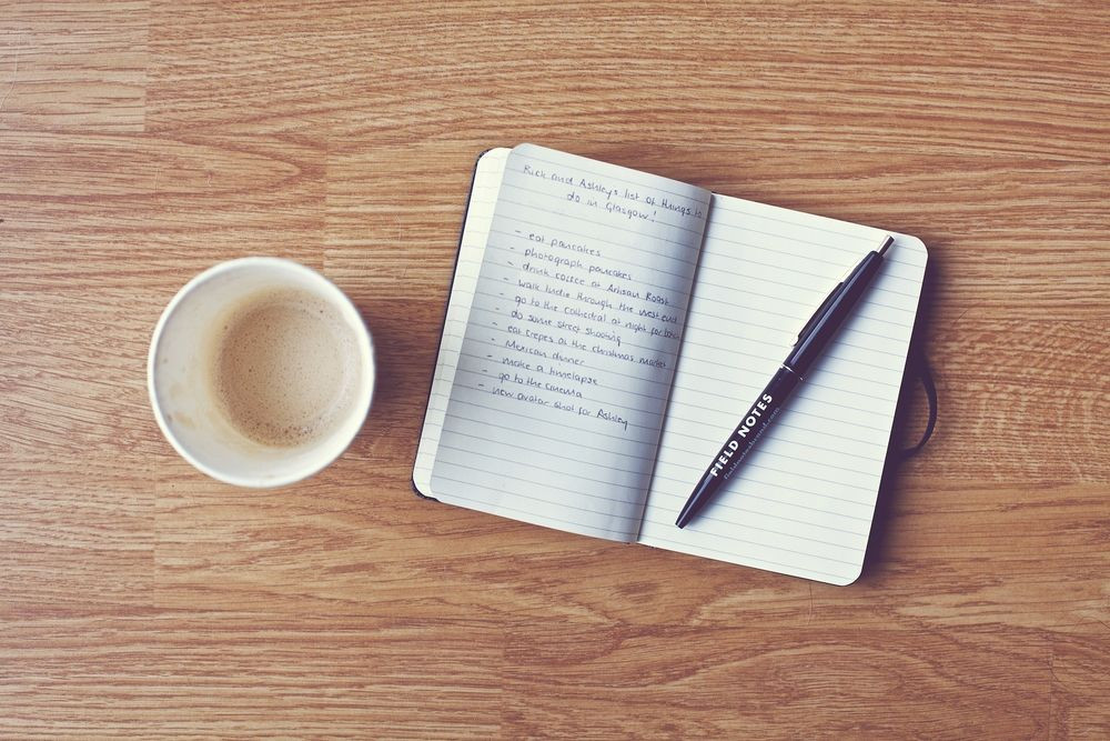 Человек пишет в книге за чашкой кофе. Изображение с публикацией, пером и текстом.