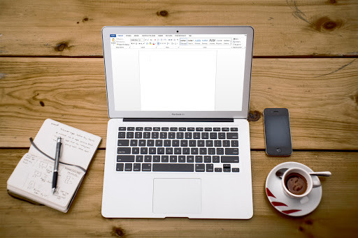 Ноутбук на столе с клавиатурой, мобильный телефон, книга, электроника.