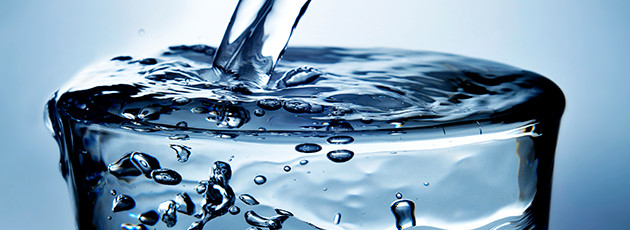 Горячая ванна с ледяными кубиками в стеклянной бутылке на фоне воды