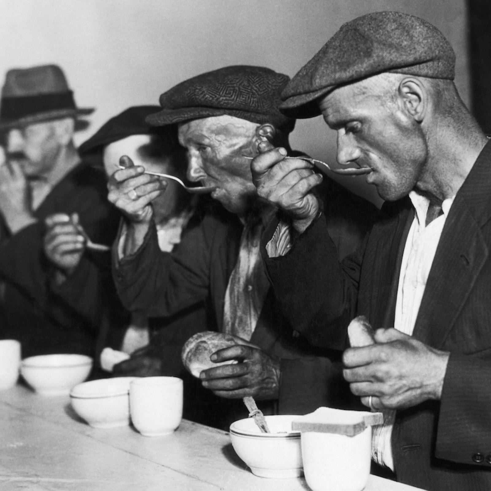 Мужчина в костюме и шляпе держит руку у лица.