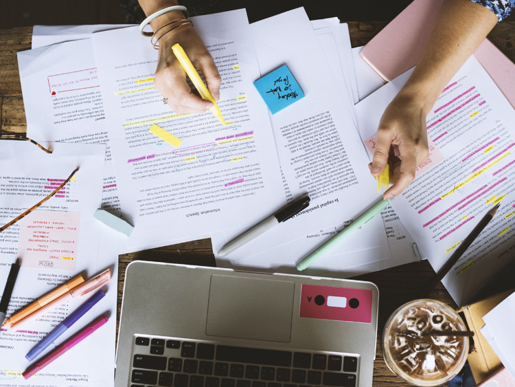 Человек работает на ноутбуке, пишет текст с помощью ручки на документе.